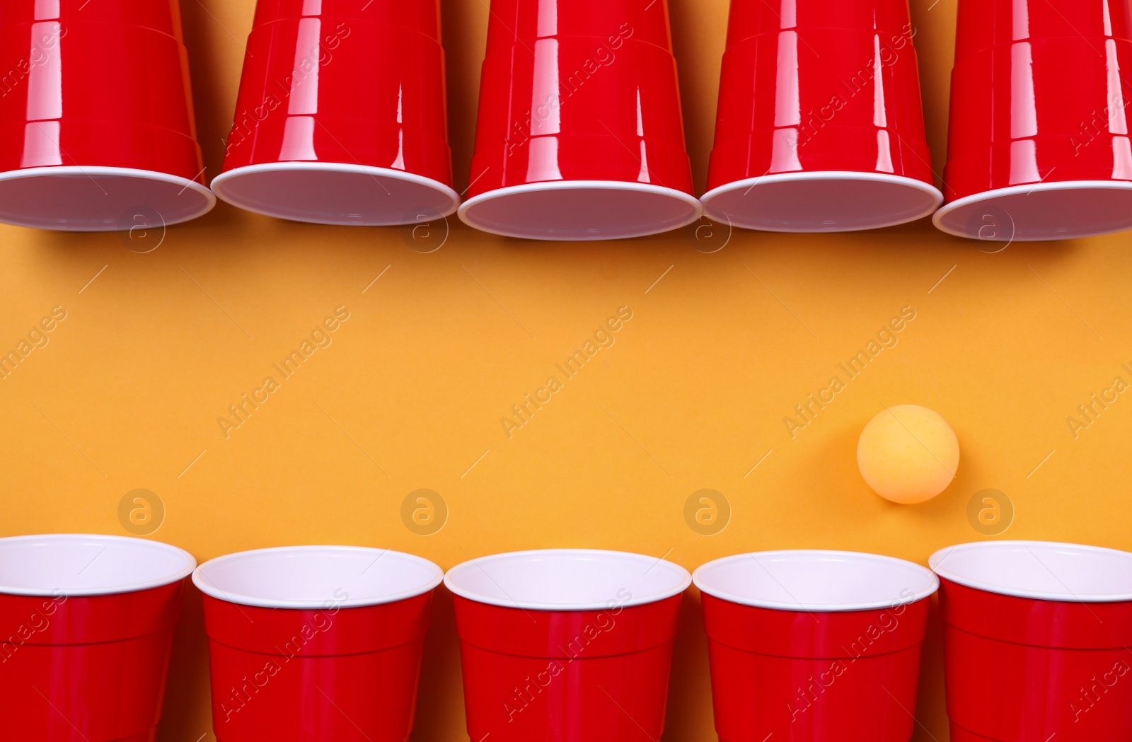 Photo of Plastic cups and ball for beer pong on orange background, flat lay