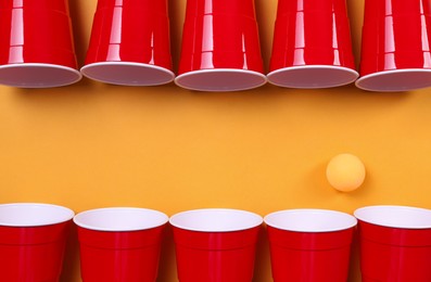 Photo of Plastic cups and ball for beer pong on orange background, flat lay