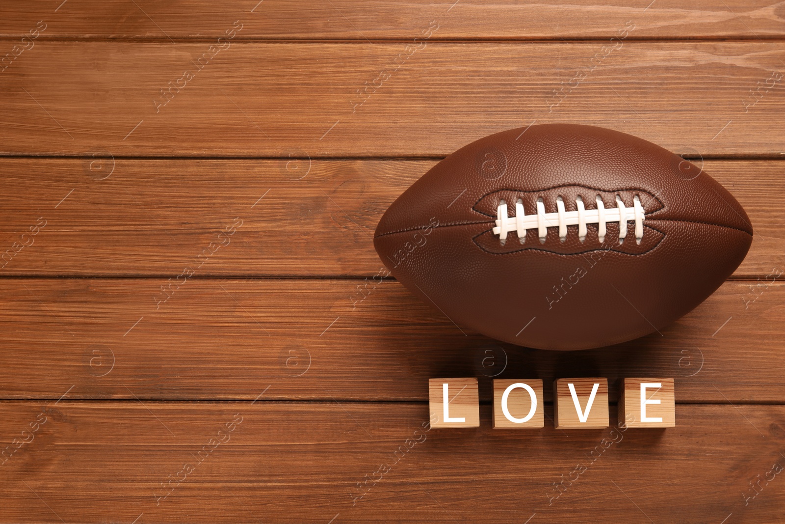 Photo of American football ball and cubes with word Love on wooden background, flat lay. Space for text