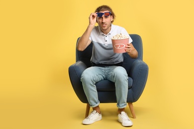 Photo of Emotional man with 3D glasses and popcorn sitting in armchair during cinema show on color background