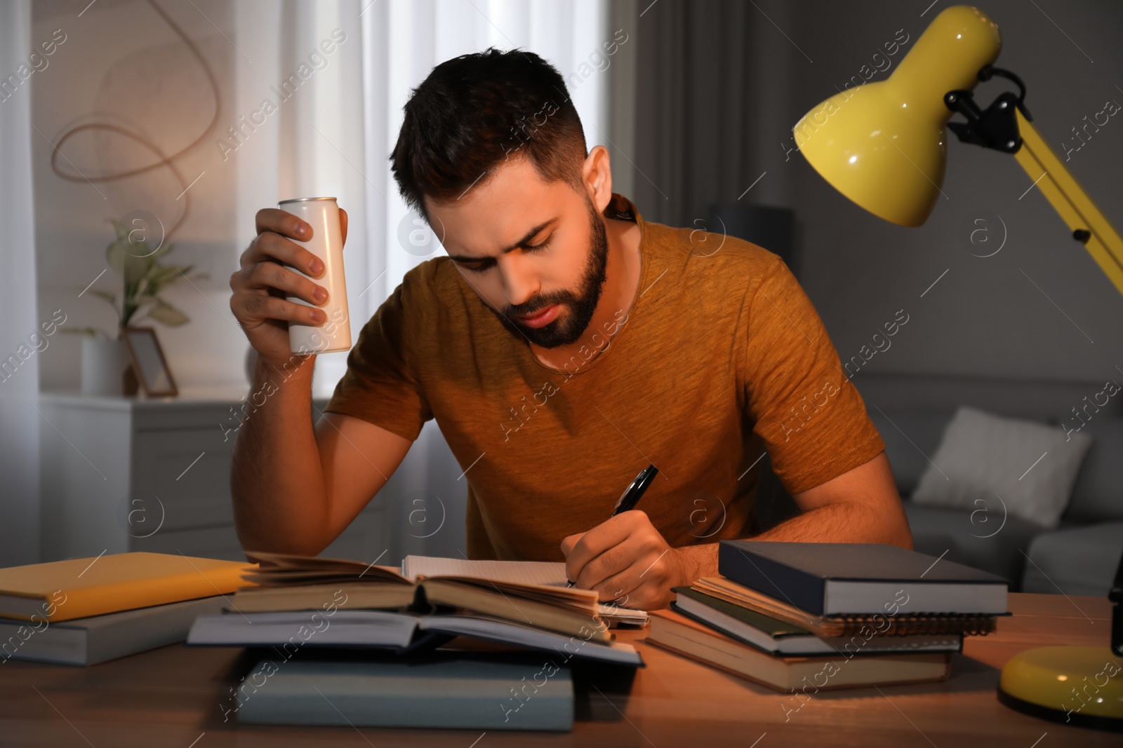 Photo of Tired young man with energy drink studying at home