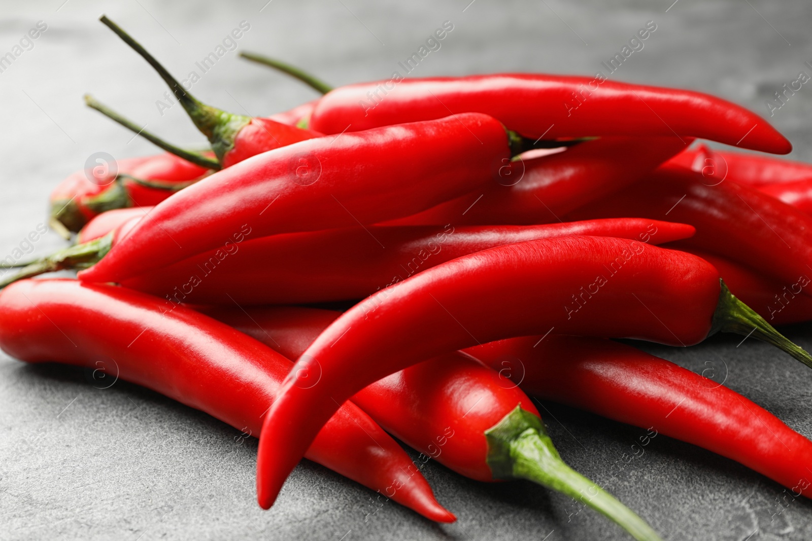 Photo of Pile of red hot chili peppers on grey table, closeup