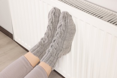 Photo of Woman warming feet near heating radiator indoors, closeup
