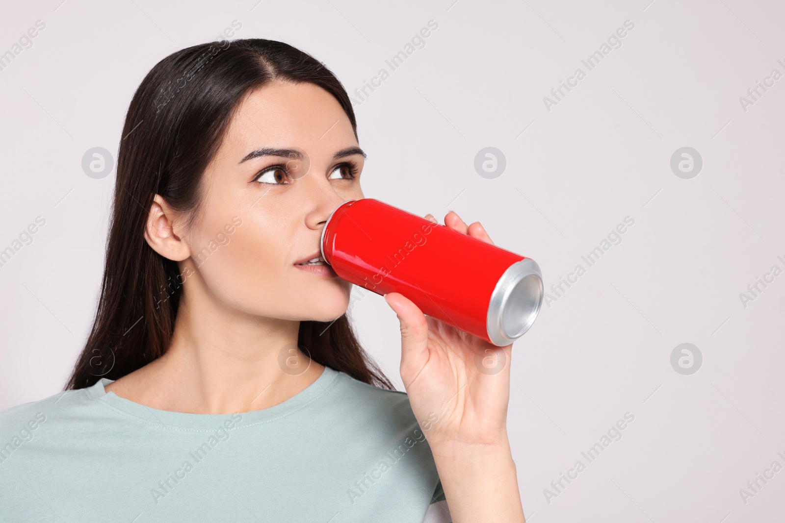 Photo of Beautiful young woman drinking from tin can on light grey background