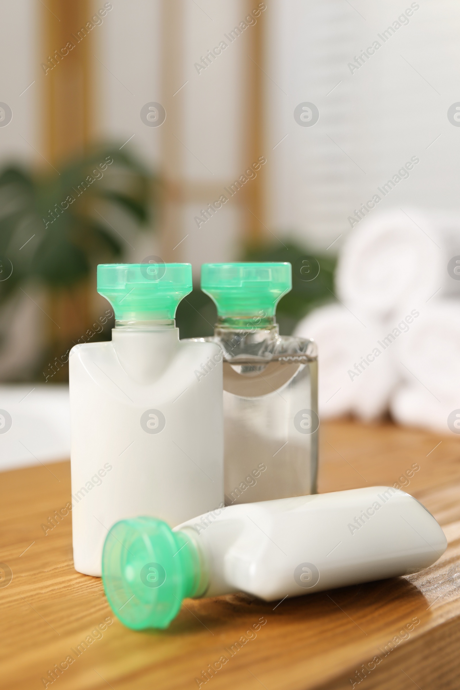 Photo of Wooden tray with mini bottles of cosmetic products on bath tub in bathroom, closeup