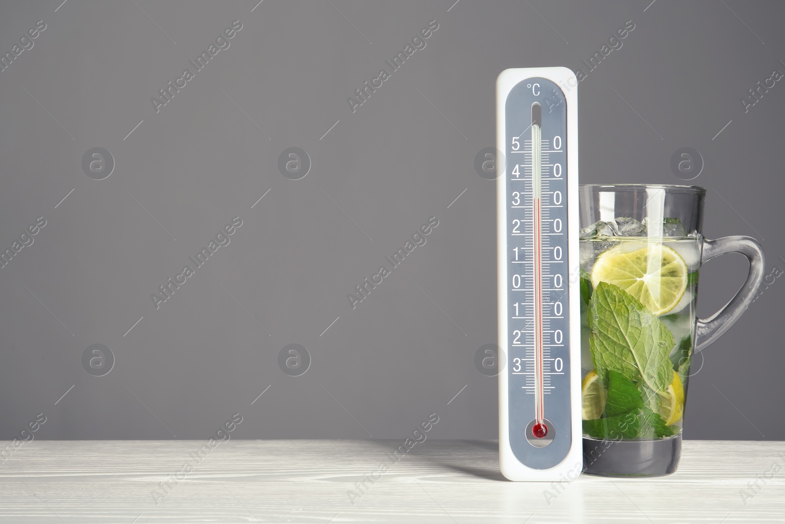 Photo of Thermometer and cup of mojito on wooden table against grey background. Space for text