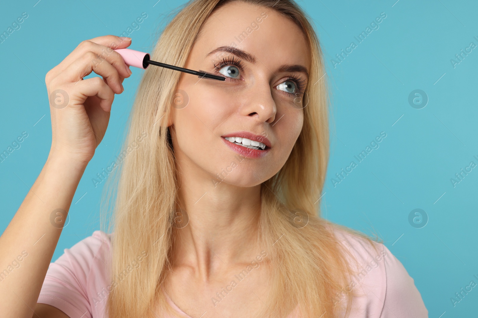 Photo of Beautiful woman applying mascara on light blue background, closeup