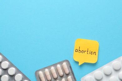 Photo of Paper note with word Abortion and pills on light blue background, flat lay. Space for text