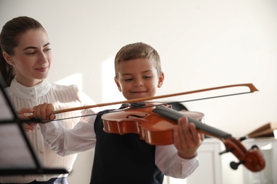 Young woman teaching little boy to play violin indoors