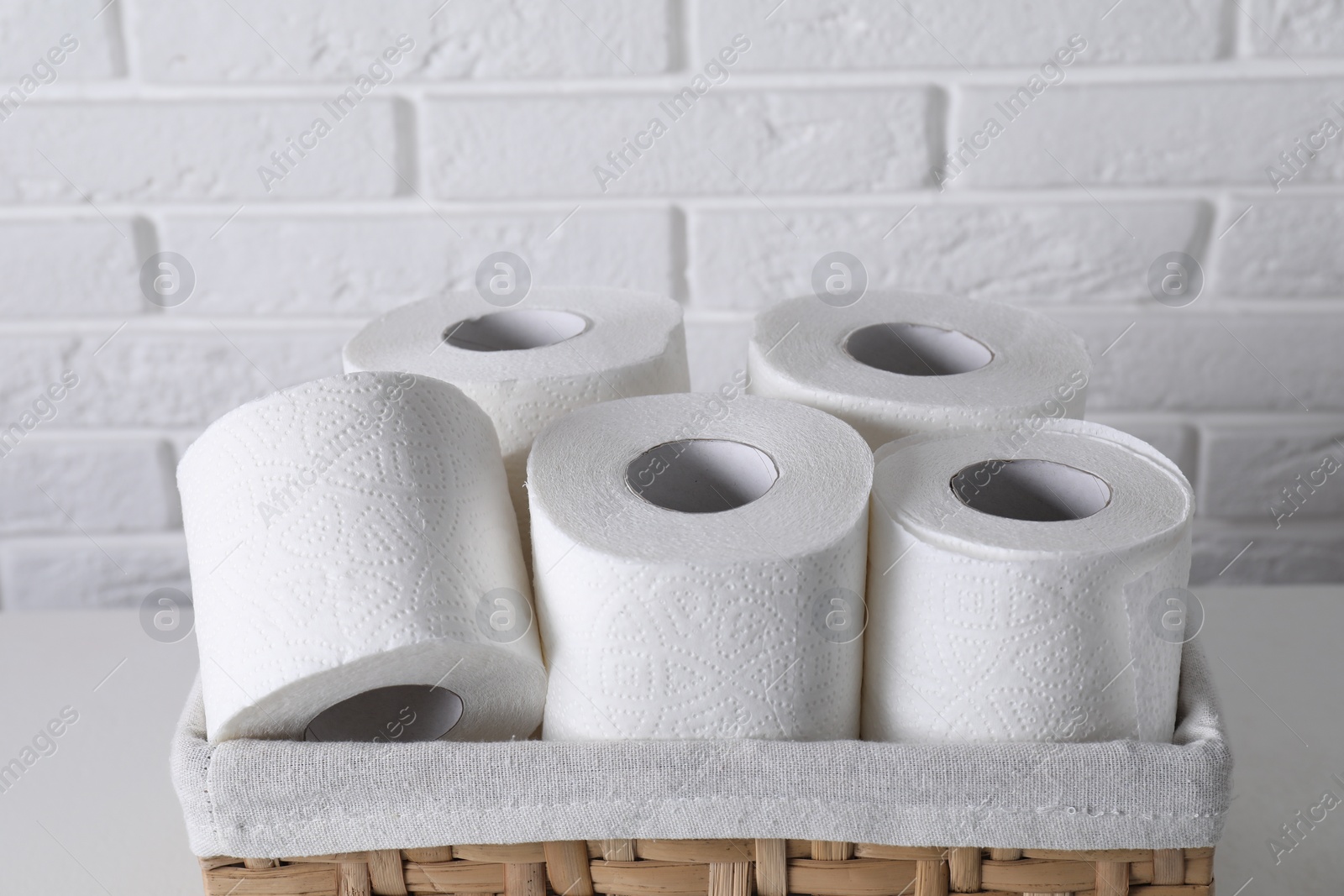 Photo of Toilet paper rolls in wicker basket on white table against brick wall