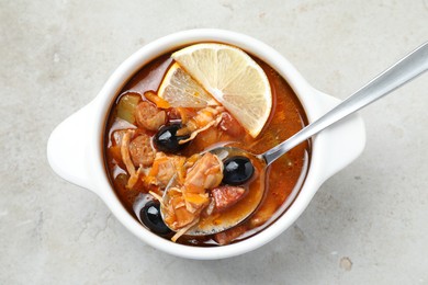 Meat solyanka soup with sausages, olives, vegetables and spoon in bowl on white textured table, top view