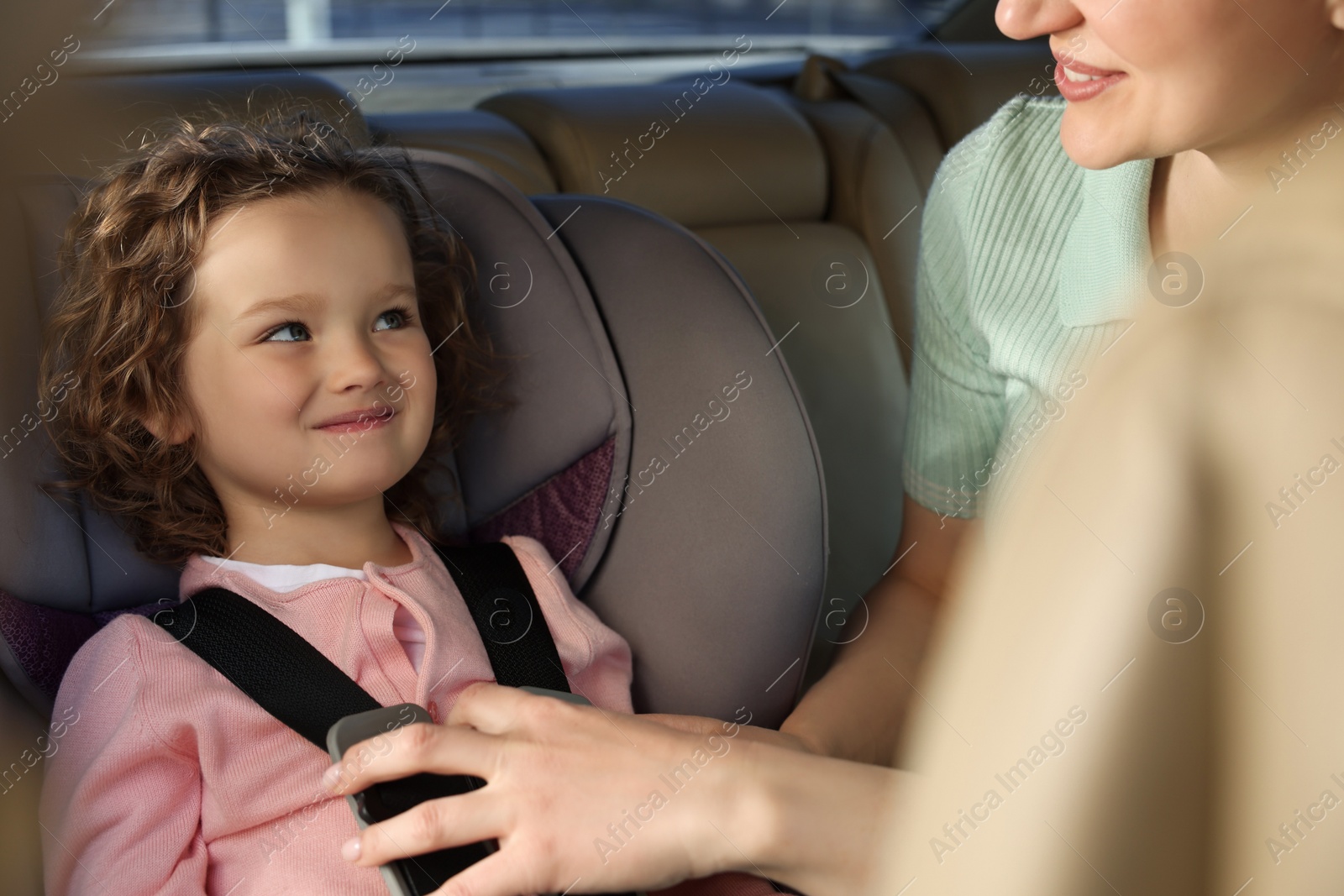 Photo of Mother fastening her daughter in child safety seat inside car