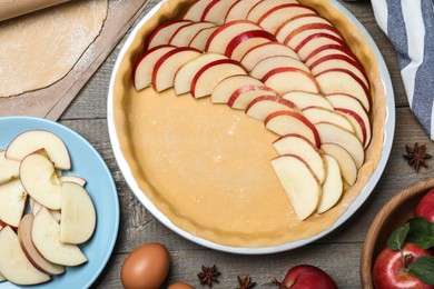 Photo of Dish with fresh apple slices and raw dough on wooden table, flat lay. Baking pie