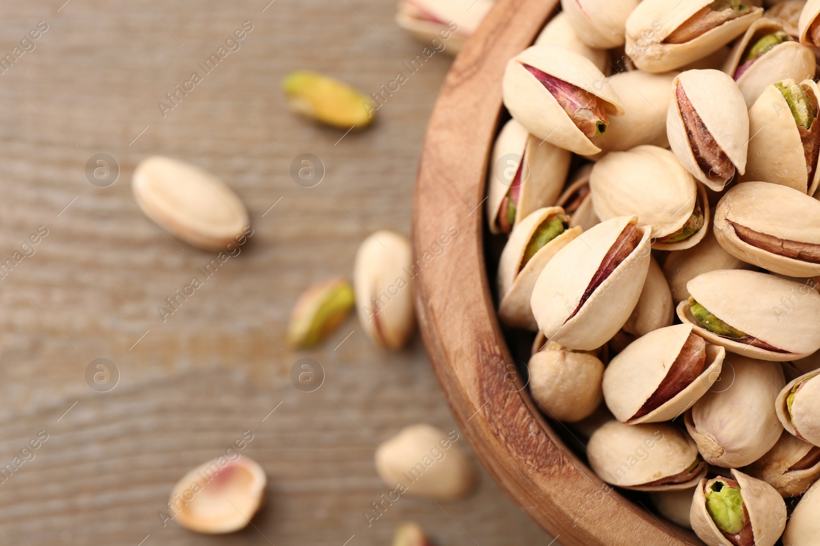 Photo of Tasty pistachios in bowl on wooden table, top view. Space for text