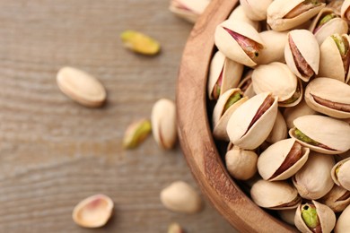 Tasty pistachios in bowl on wooden table, top view. Space for text