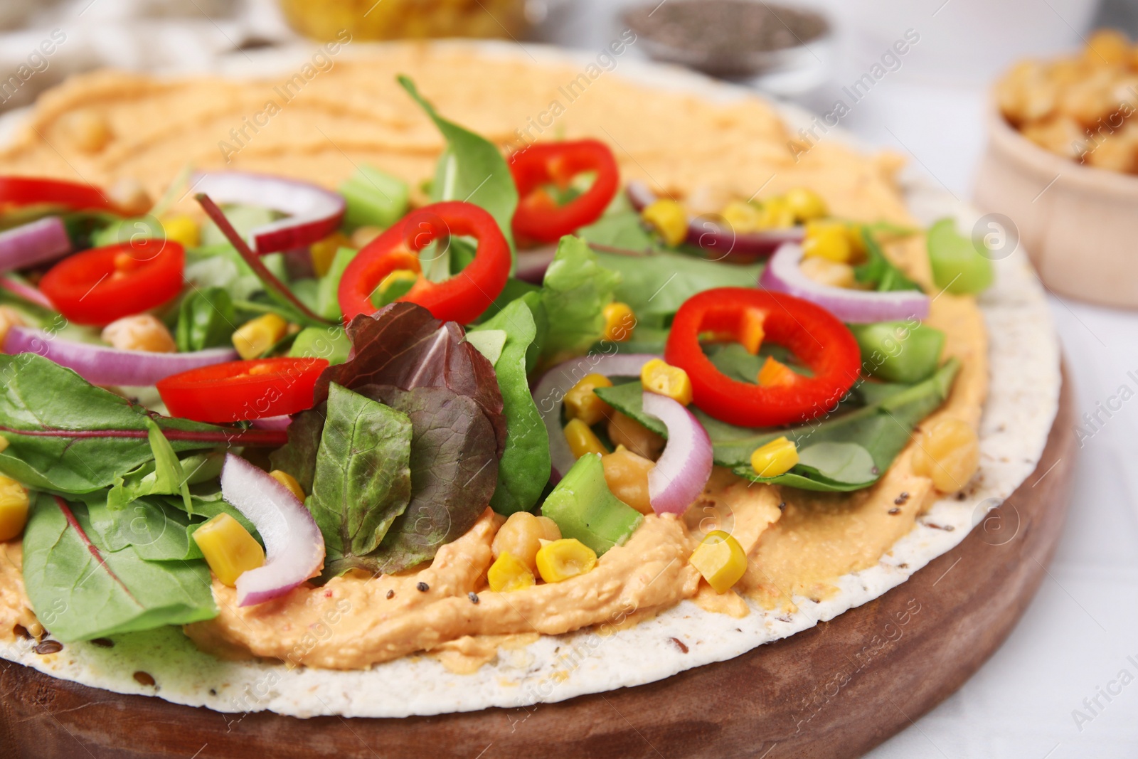 Photo of Tortilla with hummus and vegetables on table, closeup