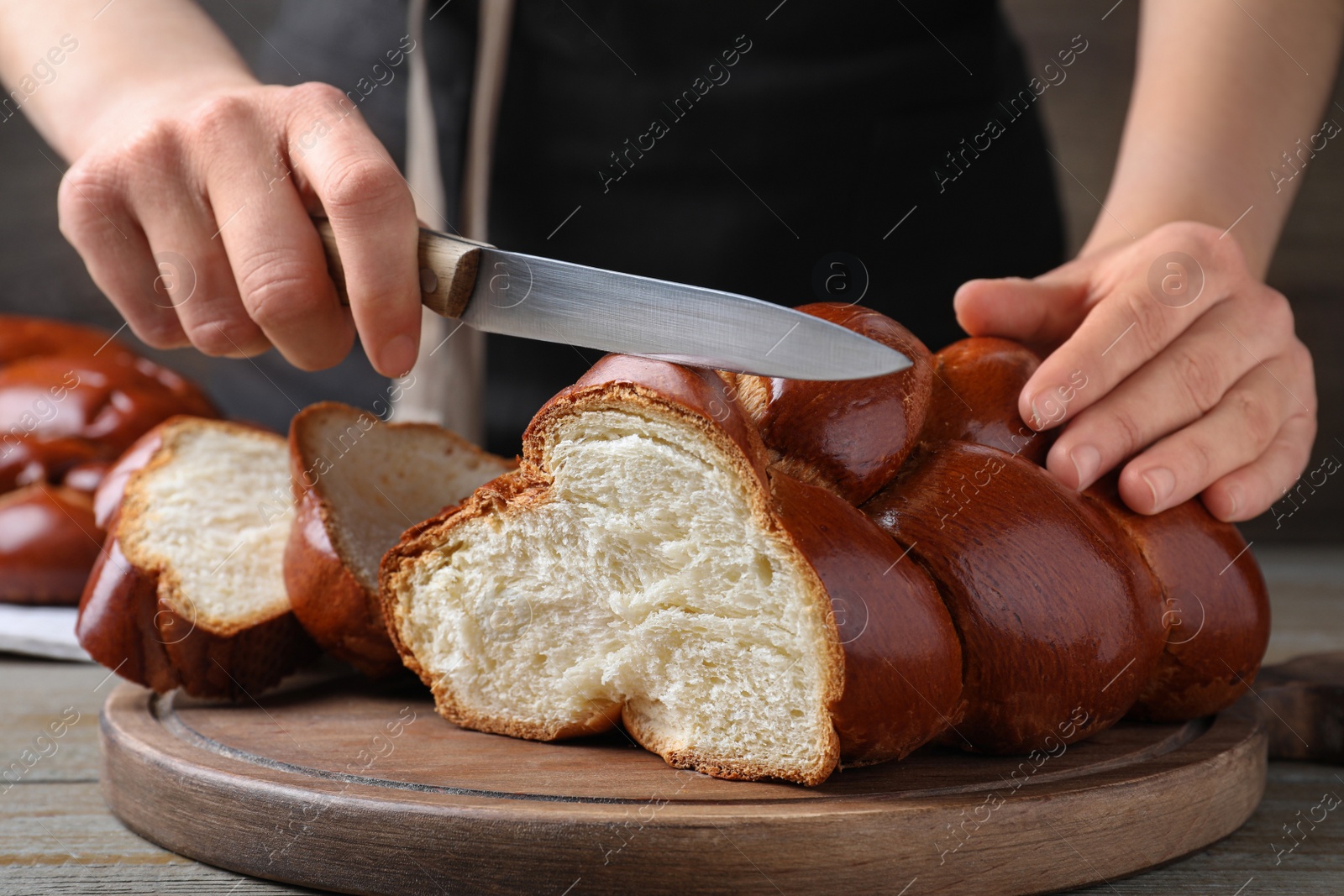 Photo of Woman cutting homemade braided bread at wooden table, closeup. Challah for Shabbat