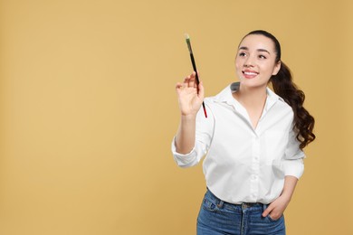 Photo of Woman with paintbrush on beige background, space for text. Young artist