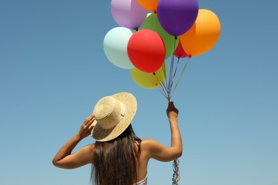 Woman with bunch of colorful balloons against blue sky, back view