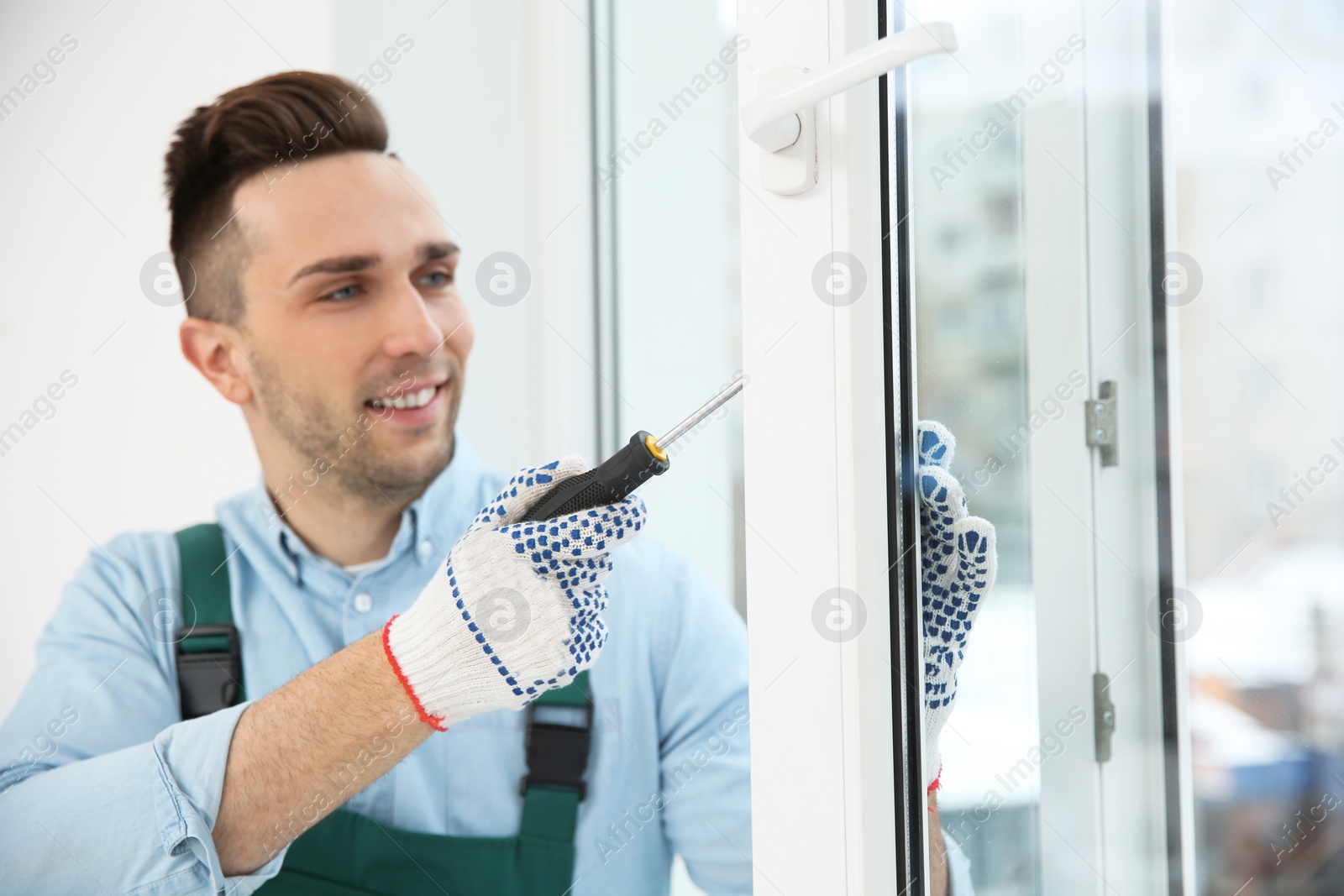 Photo of Construction worker adjusting installed window with screwdriver indoors