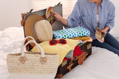 Photo of Woman packing suitcase for summer vacation in bedroom, closeup