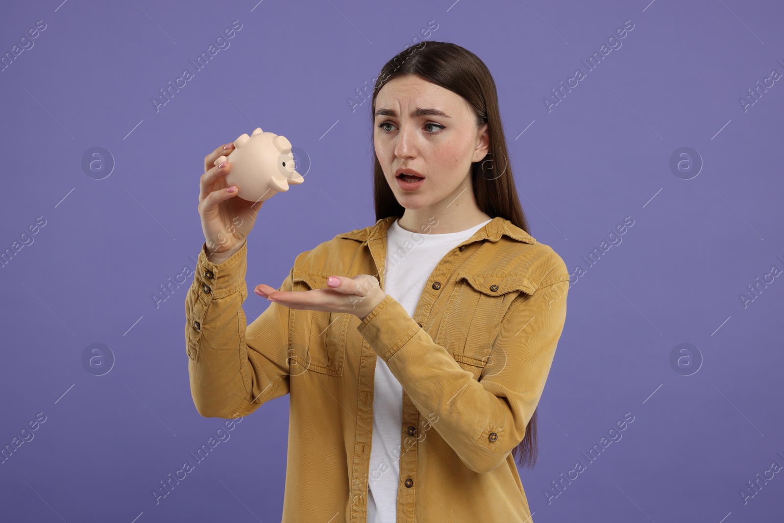 Photo of Sad woman with piggy bank on purple background