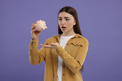 Sad woman with piggy bank on purple background