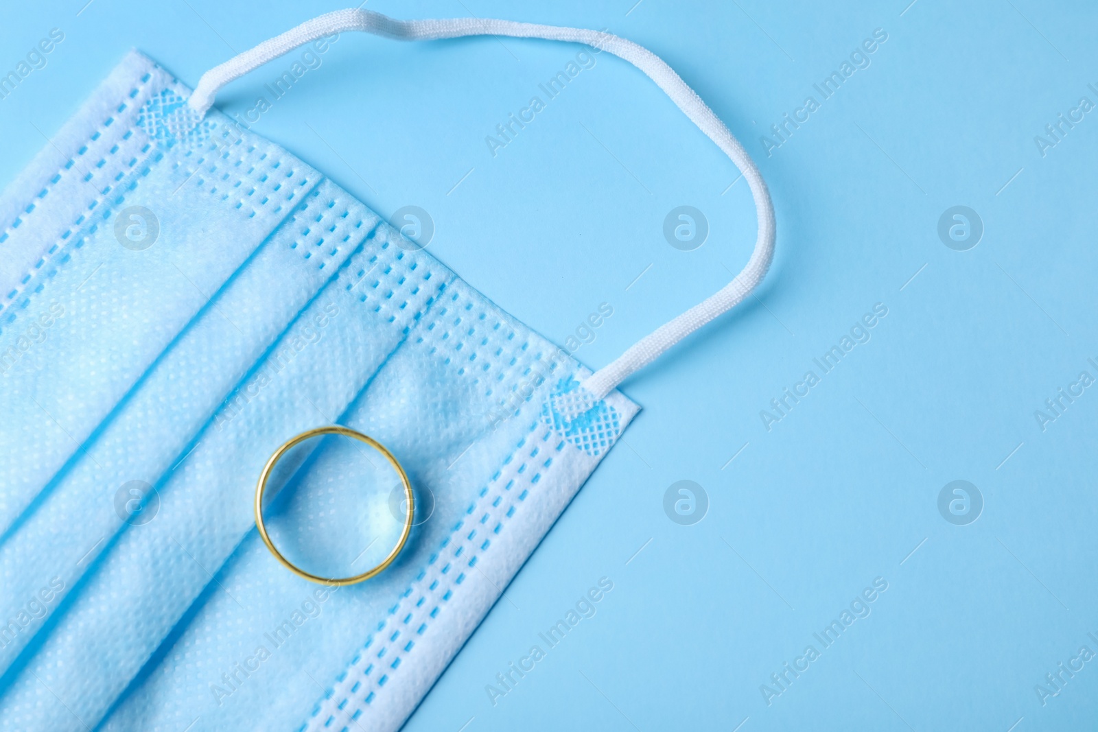 Photo of Wedding ring and medical mask on light blue background, top view with space for text. Divorce during coronavirus outbreak