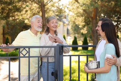 Photo of Friendly relationship with neighbours. Young family talking to elderly couple near fence outdoors