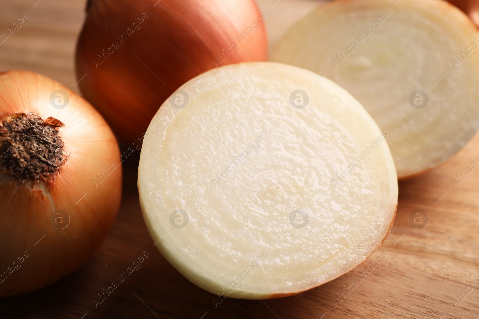Photo of Whole and cut yellow onions on wooden table, closeup