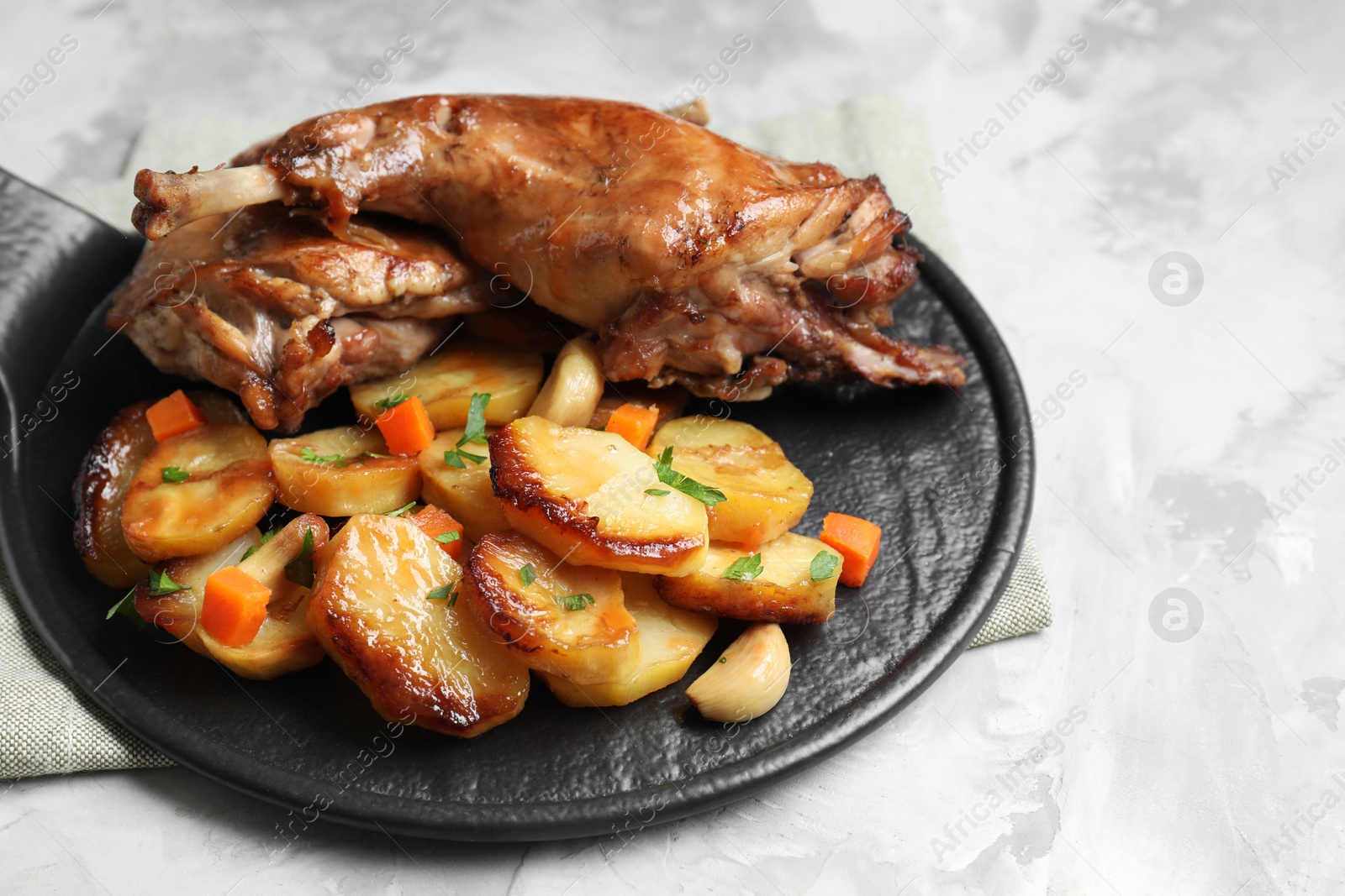 Photo of Tasty cooked rabbit meat with vegetables on light grey table, closeup. Space for text