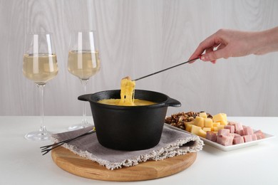 Photo of Dipping piece of ham into fondue pot with tasty melted cheese at white table, closeup