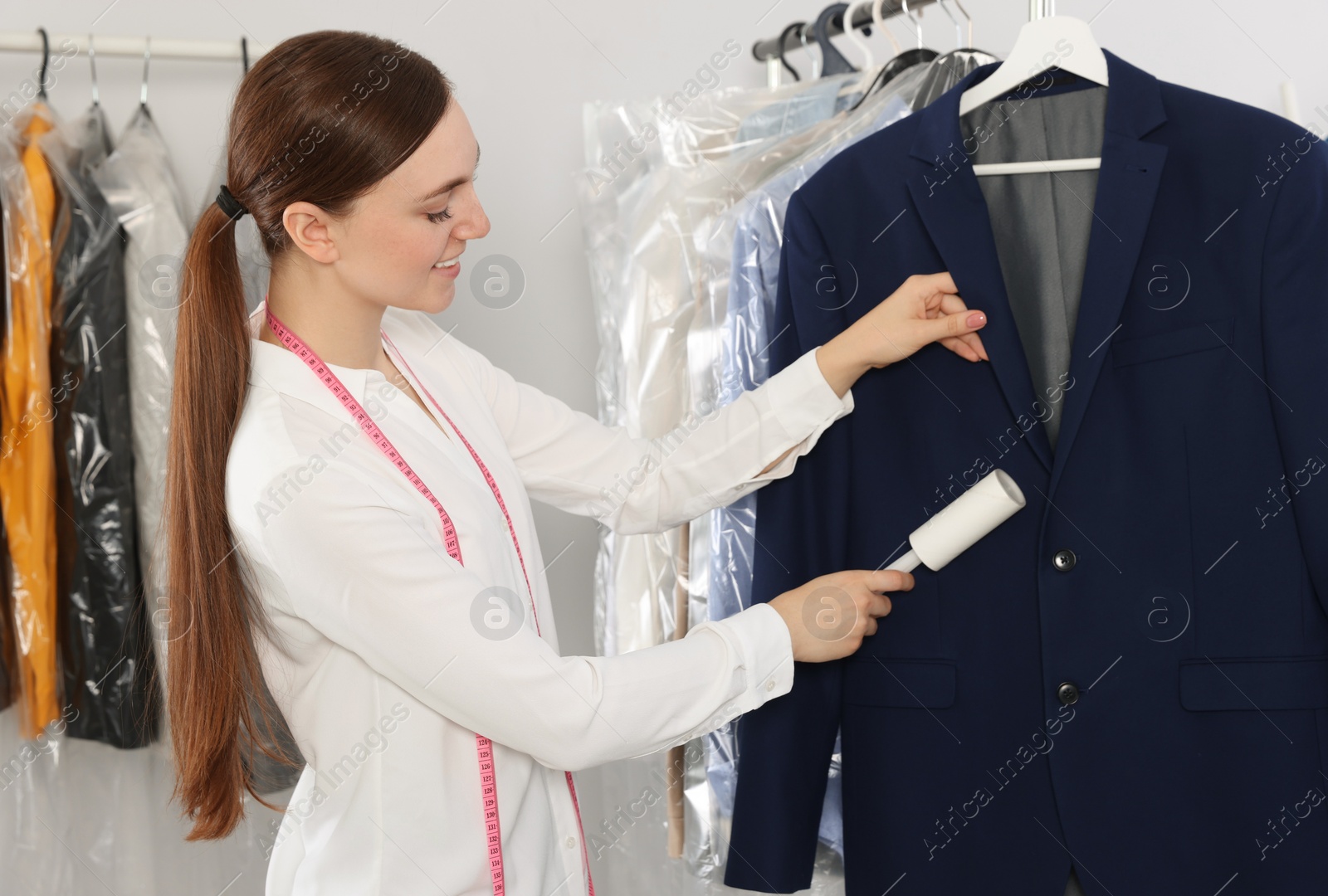 Photo of Young woman using adhesive lint roller at dry-cleaner's