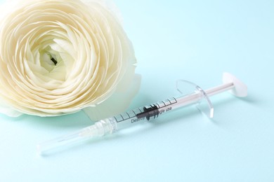 Photo of Cosmetology. Medical syringe and ranunculus flower on light blue background