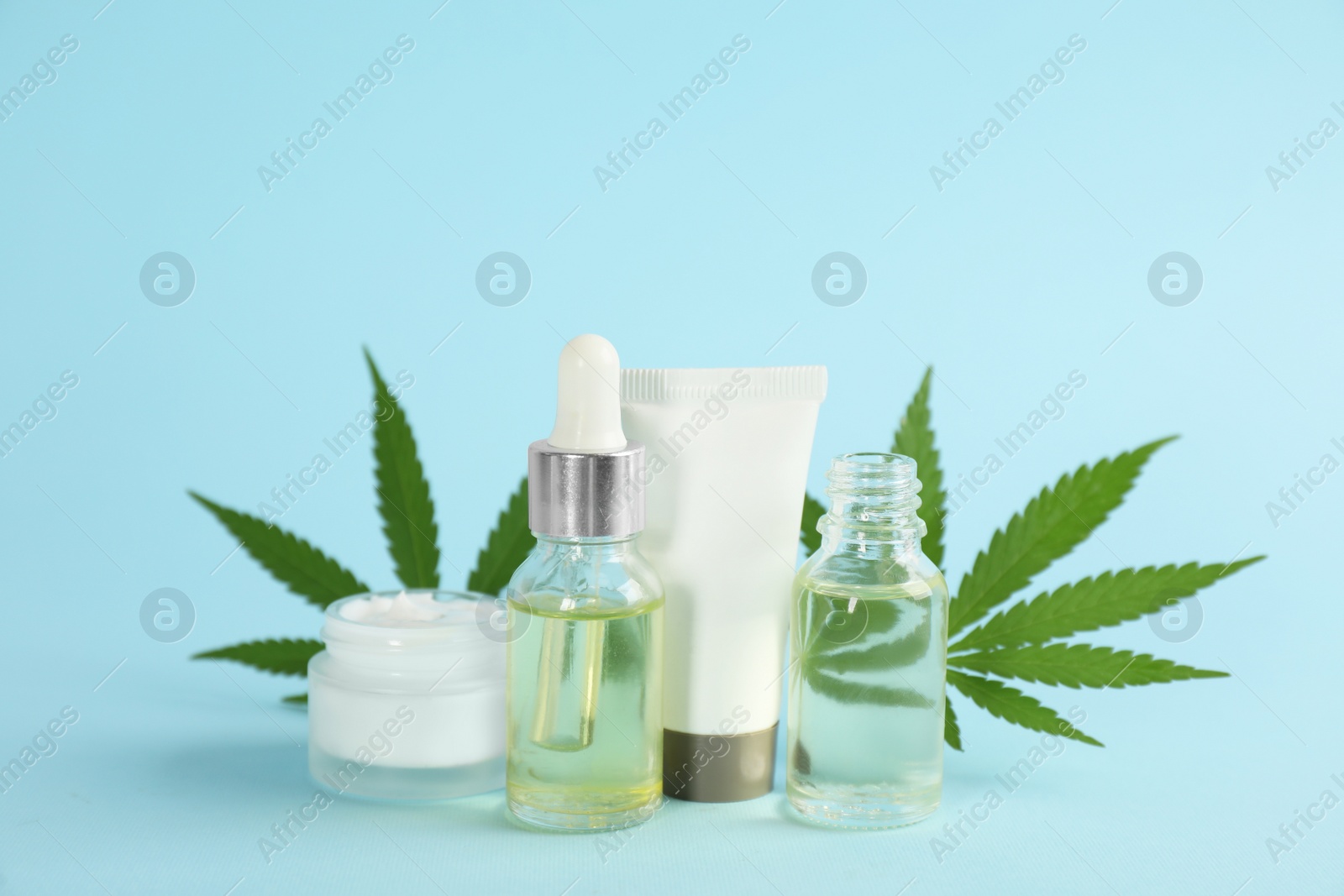 Photo of Cream, hemp leaves, bottles of CBD oil and THC tincture on light blue background