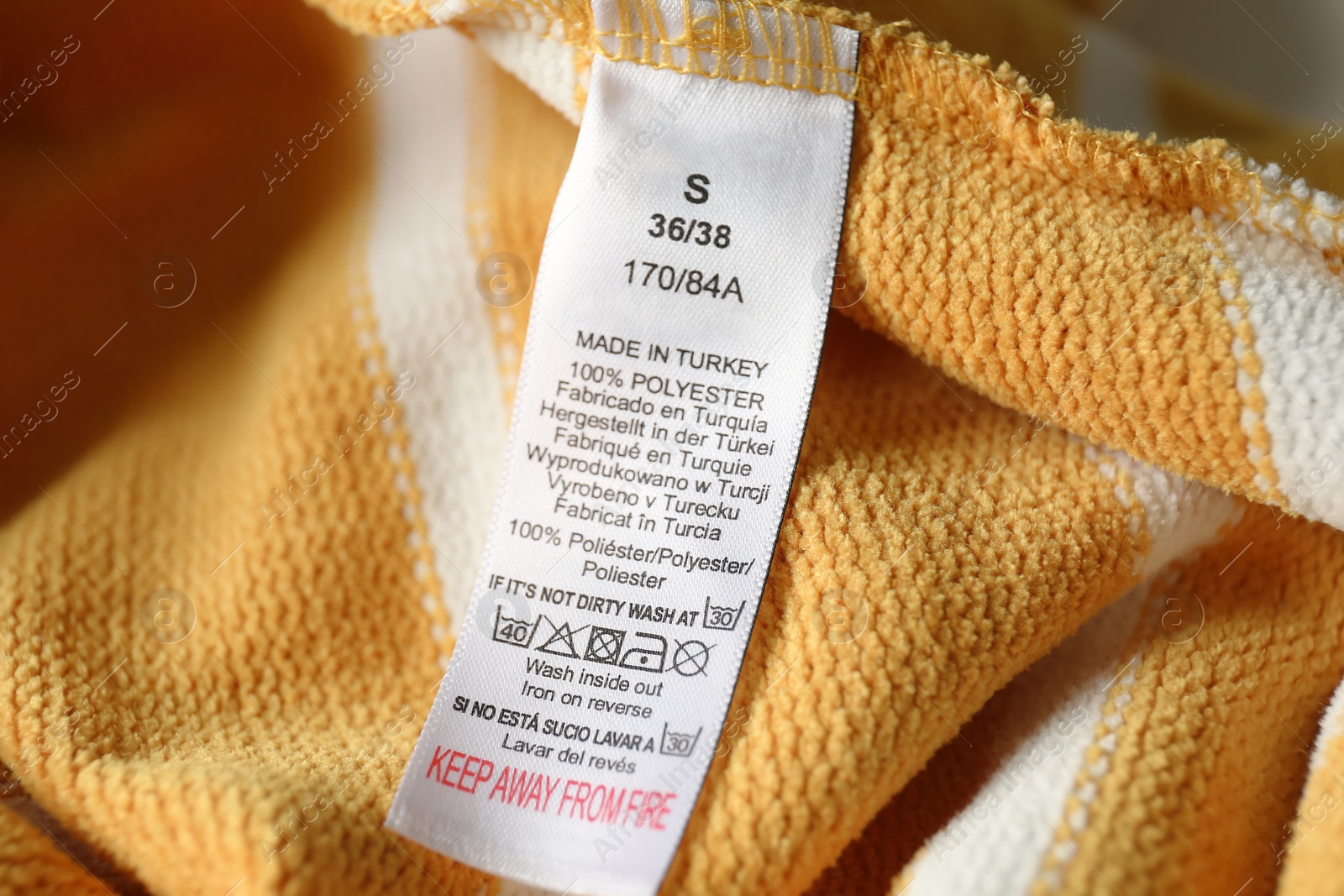 Photo of Clothing label with care symbols and material content on yellow shirt, closeup view