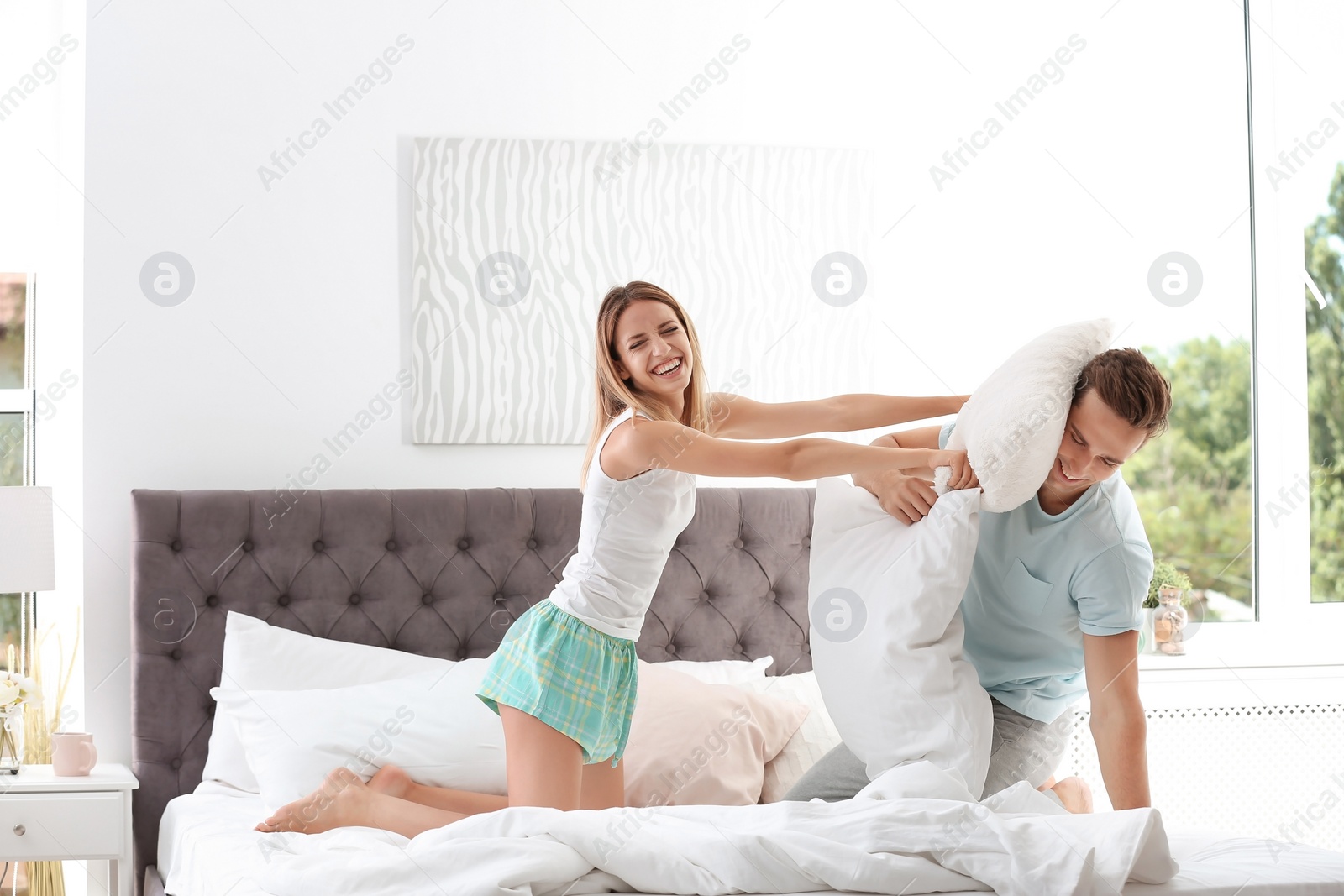 Photo of Young couple having pillow fight in bed at home