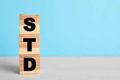 Photo of Abbreviation STD made with cubes on white wooden table against light blue background, space for text