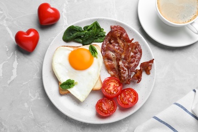 Romantic breakfast with fried bacon and heart shaped egg on grey table, flat lay. Valentine's day celebration
