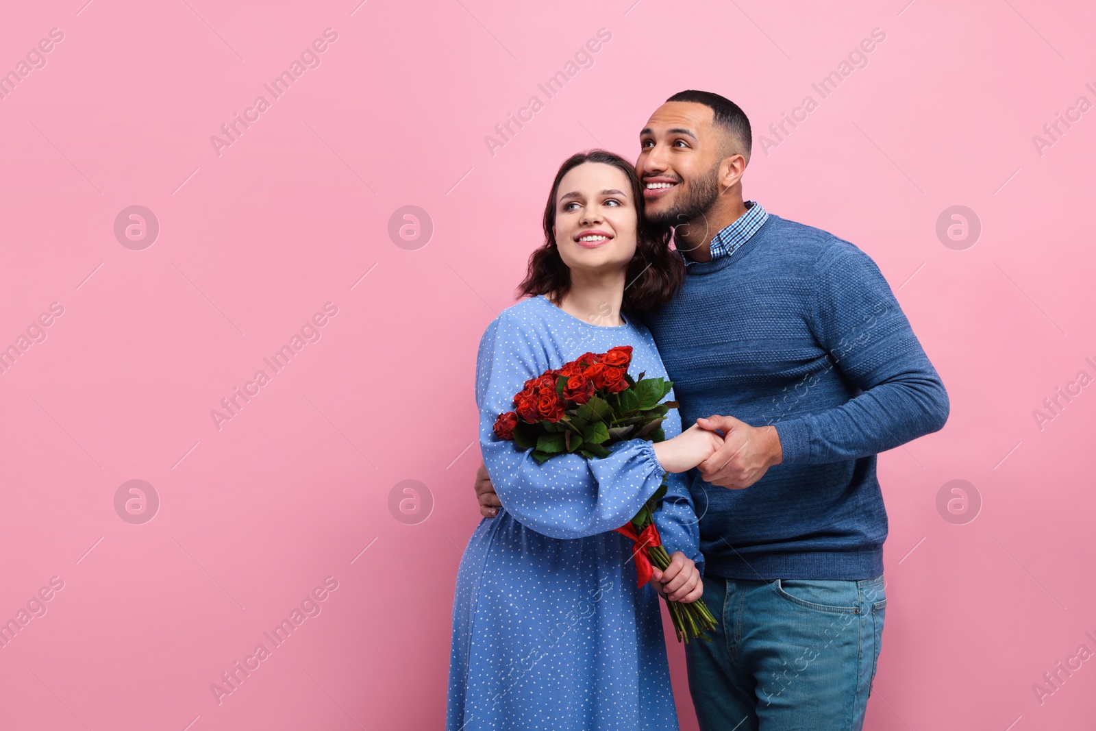 Photo of Happy couple celebrating Valentine's day. Beloved woman with bouquet of red roses on pink background, space for text