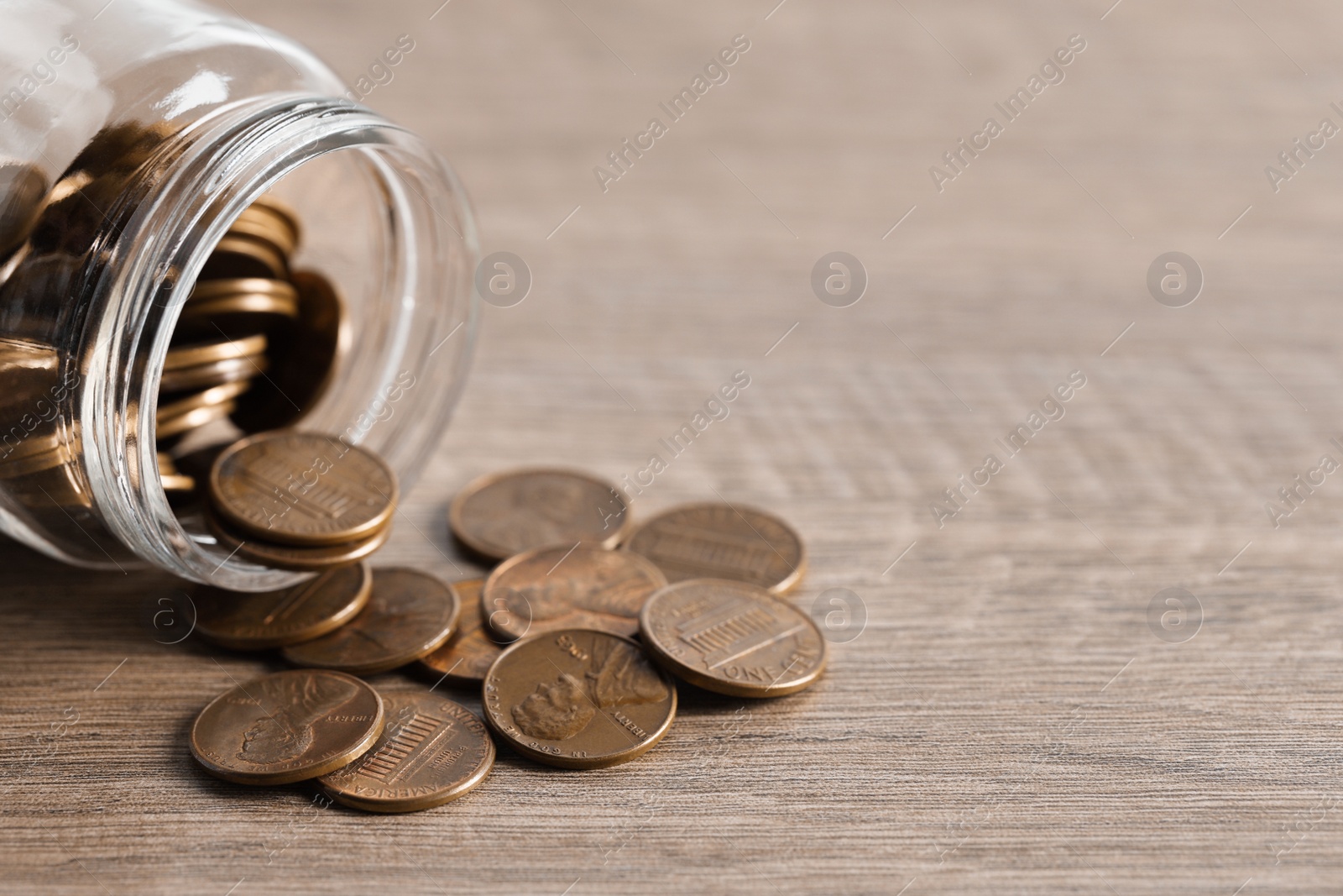 Photo of Glass jar with coins on wooden table. Space for text