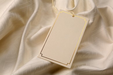 Blank tag on beige fabric, above view. Space for text