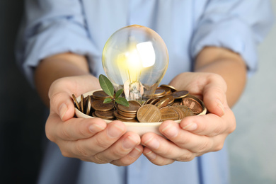 Photo of Woman with coins, light bulb and green plant, closeup. Power saving