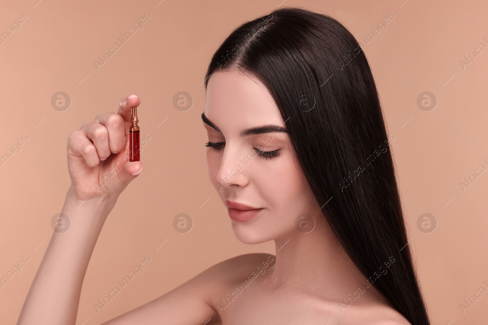 Photo of Beautiful young woman holding skincare ampoule on beige background