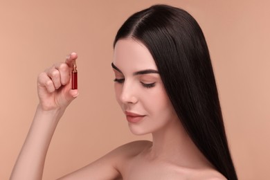 Beautiful young woman holding skincare ampoule on beige background