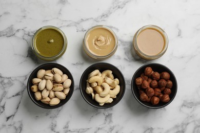 Photo of Jars with butters made of different nuts and ingredients on white marble table, flat lay