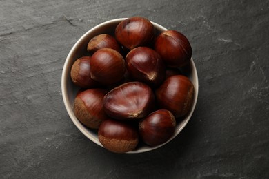 Photo of Roasted edible sweet chestnuts in bowl on grey textured table, top view