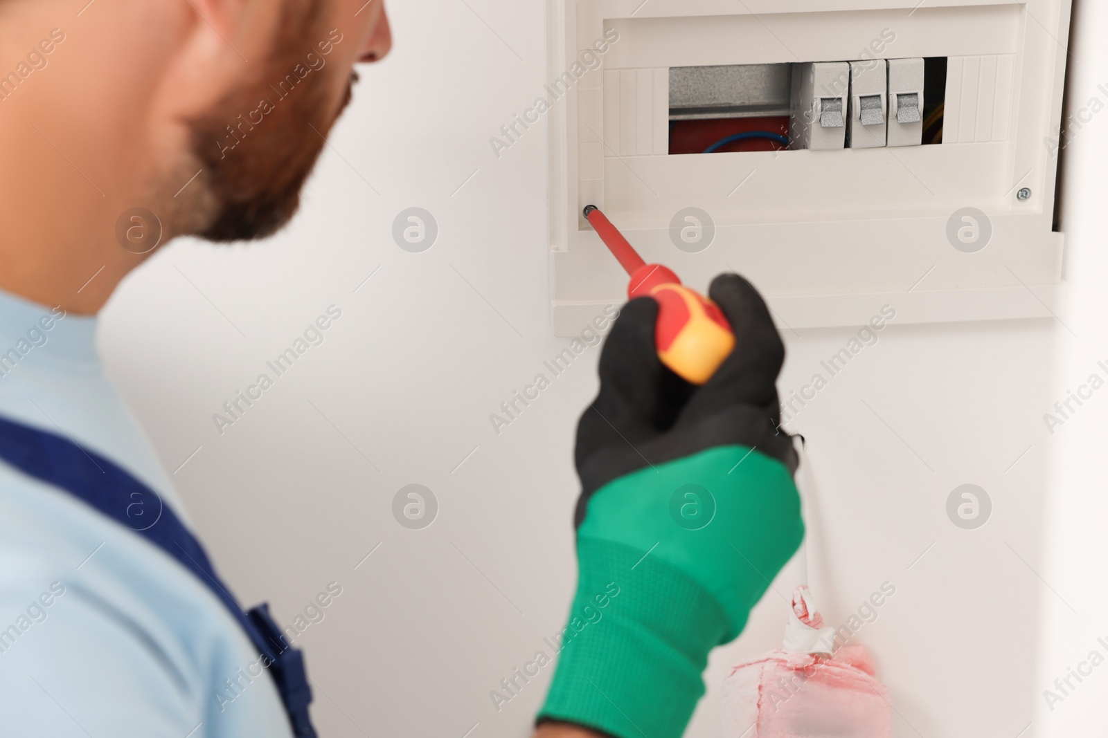 Photo of Electrician installing fuse box with screwdriver indoors