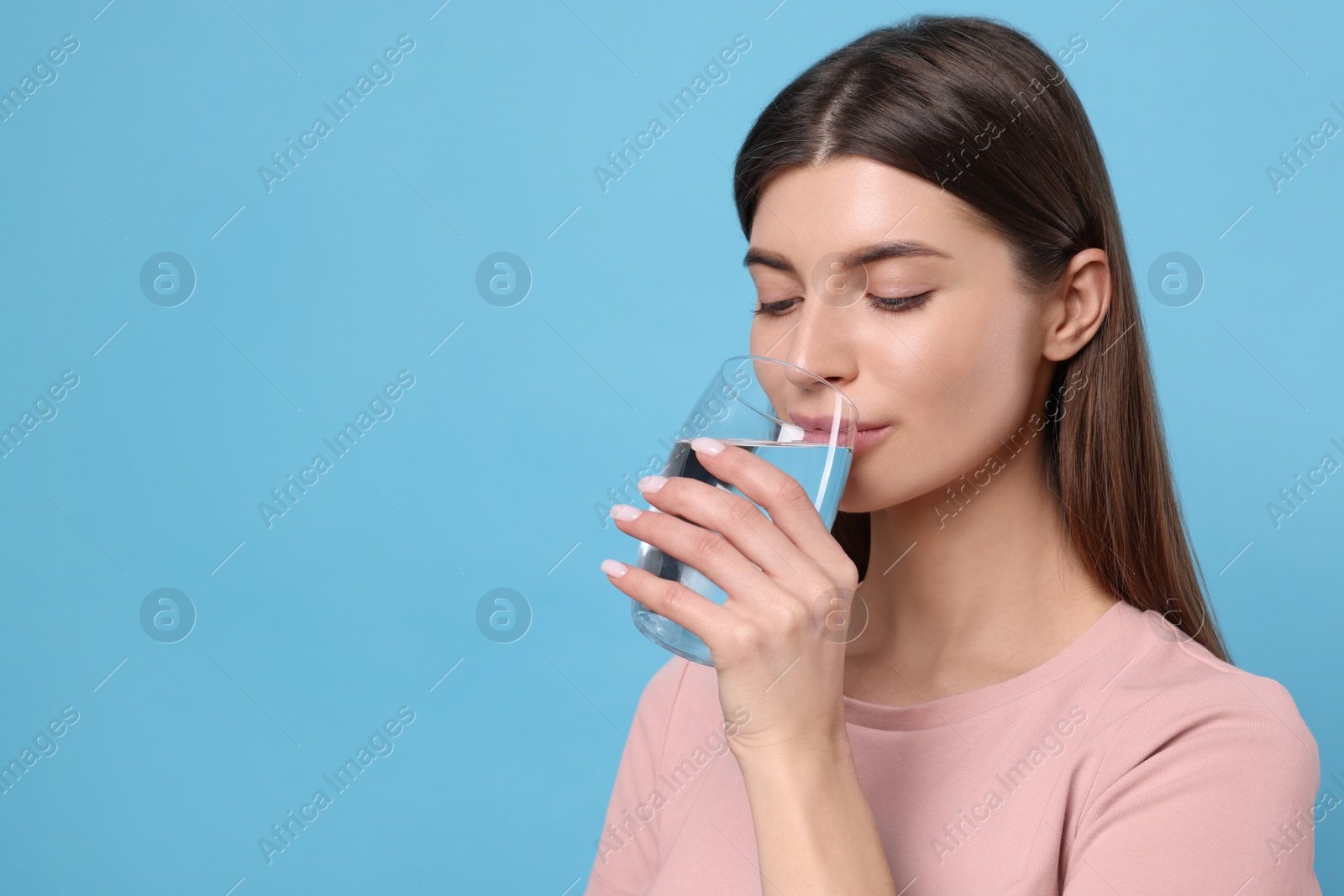 Photo of Healthy habit. Woman drinking fresh water from glass on light blue background. Space for text