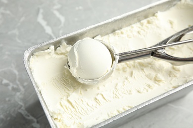 Container and scoop with delicious vanilla ice cream on table, closeup